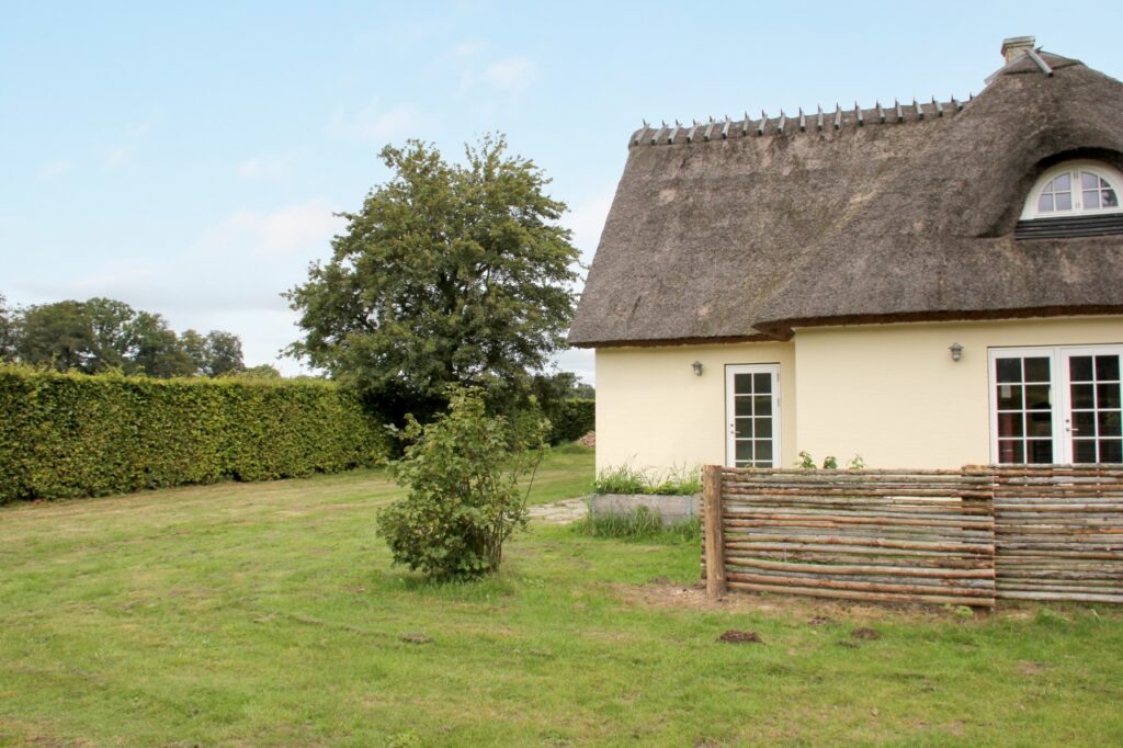 Hvidt stråtækt hus med grøn have og træer omkring