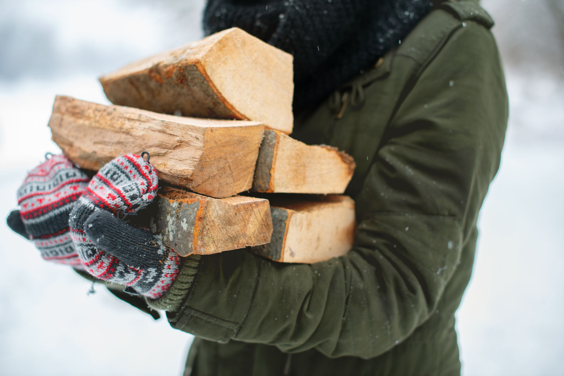 Person i vintertøj bærer en favn brænde i sneen