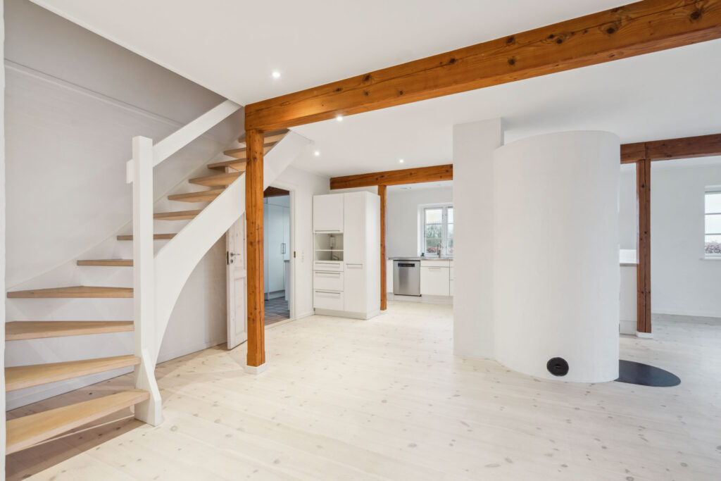 Moderne lys stue med træbjælker og trappe i landlig stil