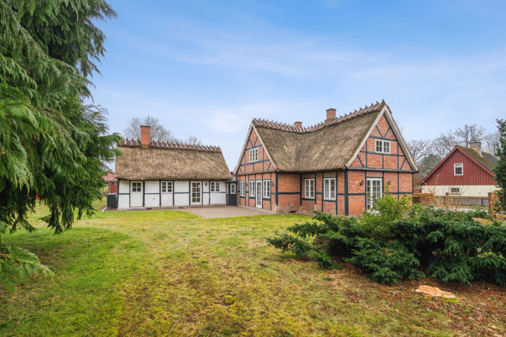 Stråtækt bindingsværkshus i grønne omgivelser under blå himmel